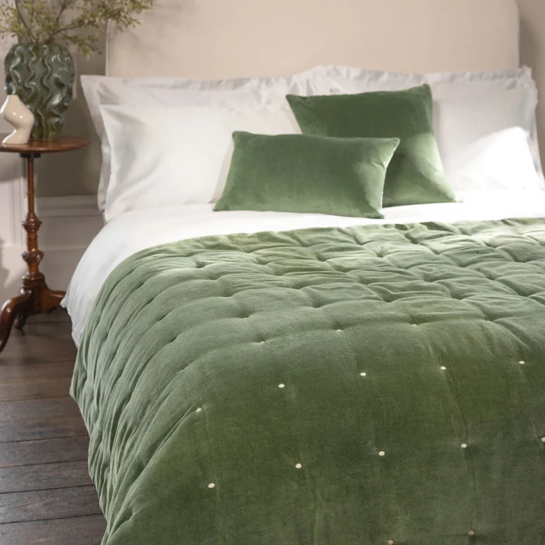 Green quilted comforter on a bed with white pillows in a bedroom setting.