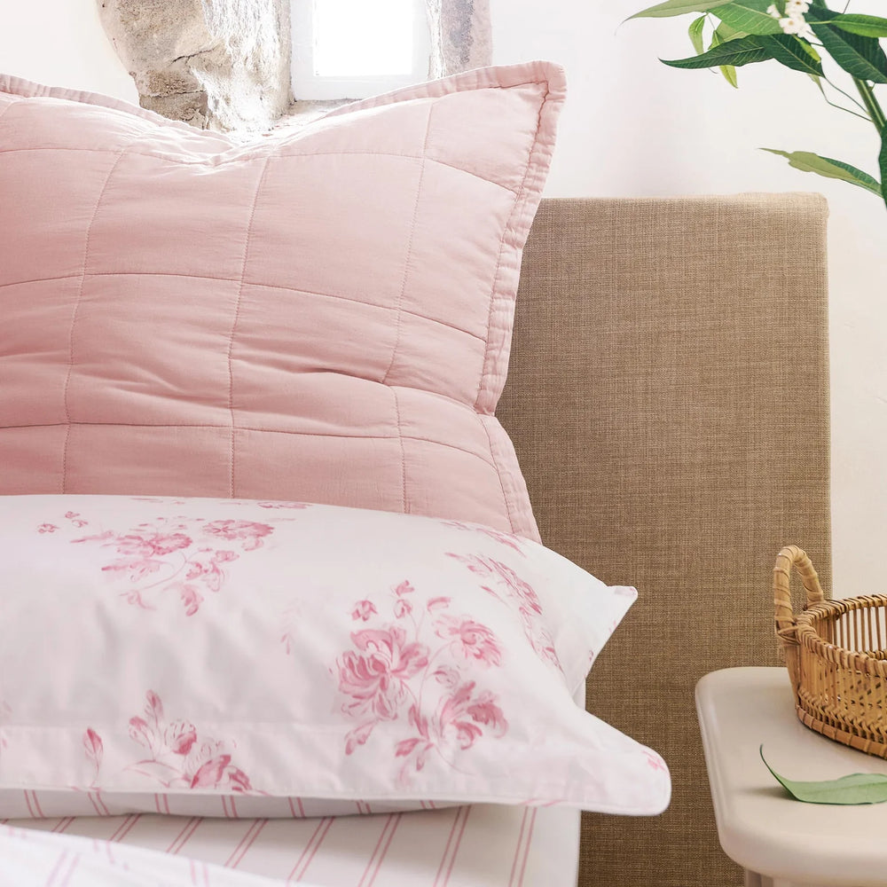 Pink floral bedding on a bed with a wicker basket and plant in the background