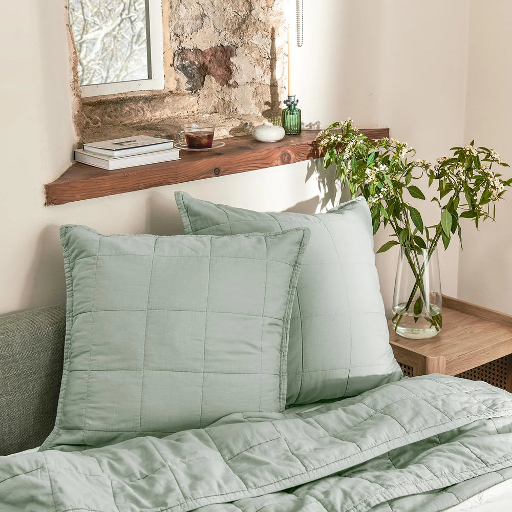 Green bedding set on a bed with a wooden shelf in the background