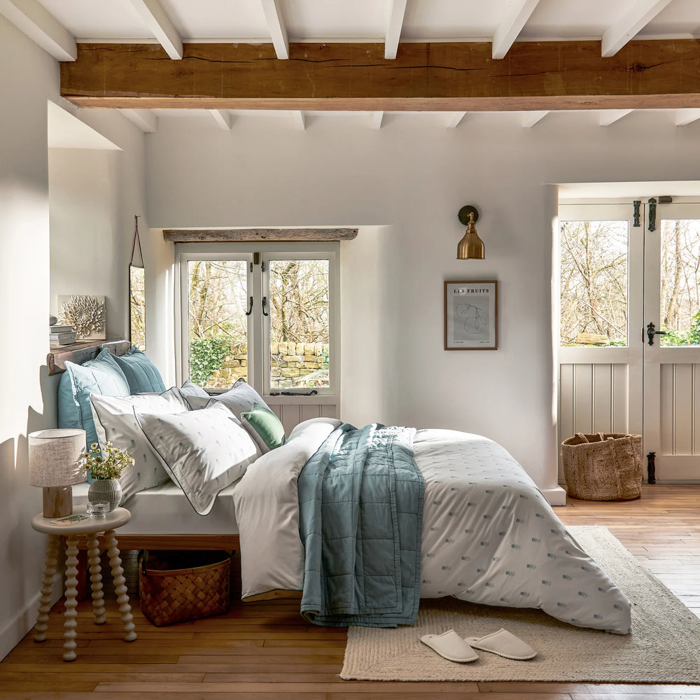 Cozy bedroom with wooden beams, a bed with teal and white bedding, and a small table with a lamp.