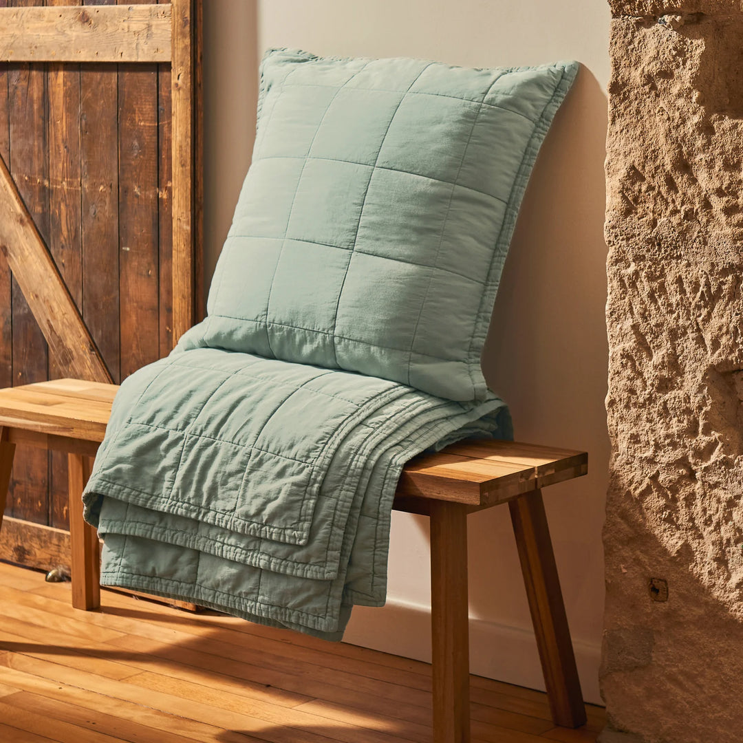Green quilt draped over a wooden bench against a rustic stone wall.