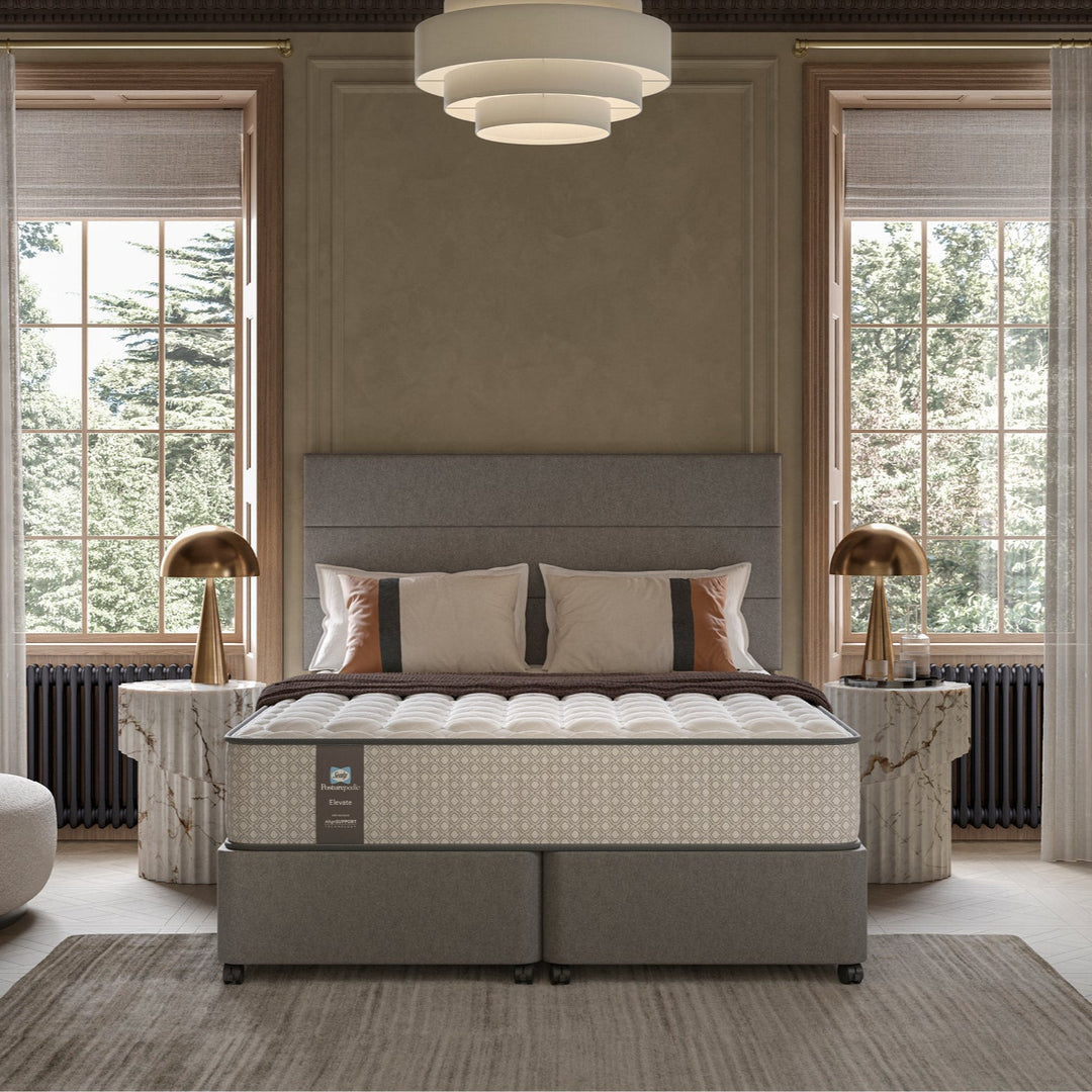 Hotel bedroom with a large bed with a Sealy Monarch mattress in the center, flanked by two lamps and a rug.