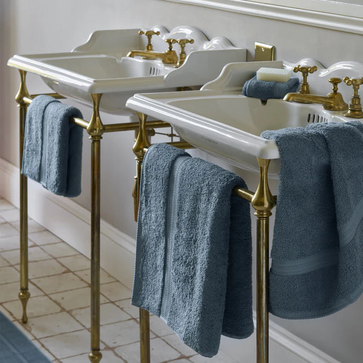 Bathroom sinks with gold fixtures and blue towels on a tiled floor.