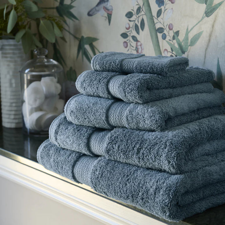 Stack of CHRISTY Renaissance Towels - Denim on a surface with decorative items in the background