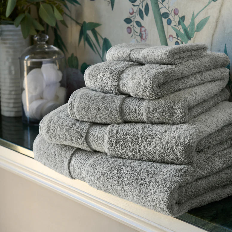Stack of CHRISTY Renaissance Towels - Dove Grey on a surface with decorative items in the background