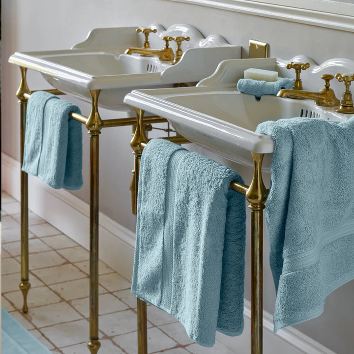 Bathroom sinks with gold fixtures and CHRISTY Renaissance Towels - Soft Chambray on a tiled floor.
