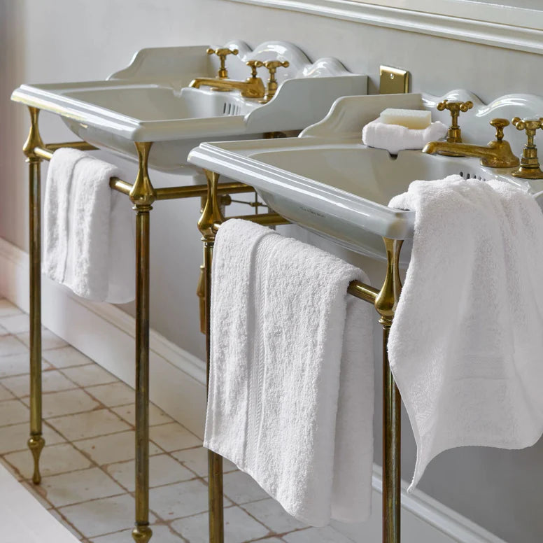 Two white sinks with gold fixtures and CHRISTY Renaissance Towels - White in a bathroom setting.