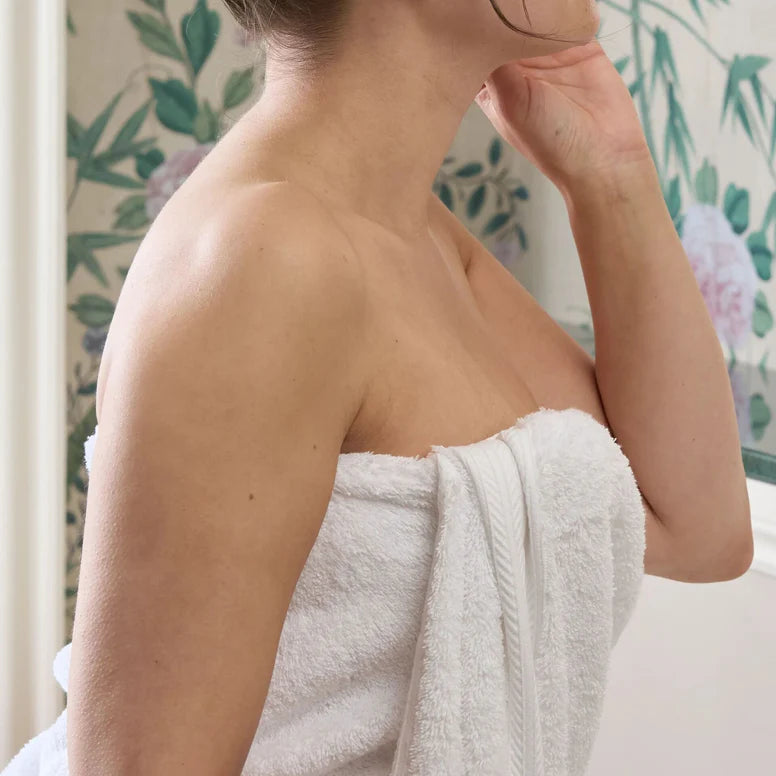 Person wrapped in CHRISTY Renaissance Towels - White with a floral-patterned curtain in the background