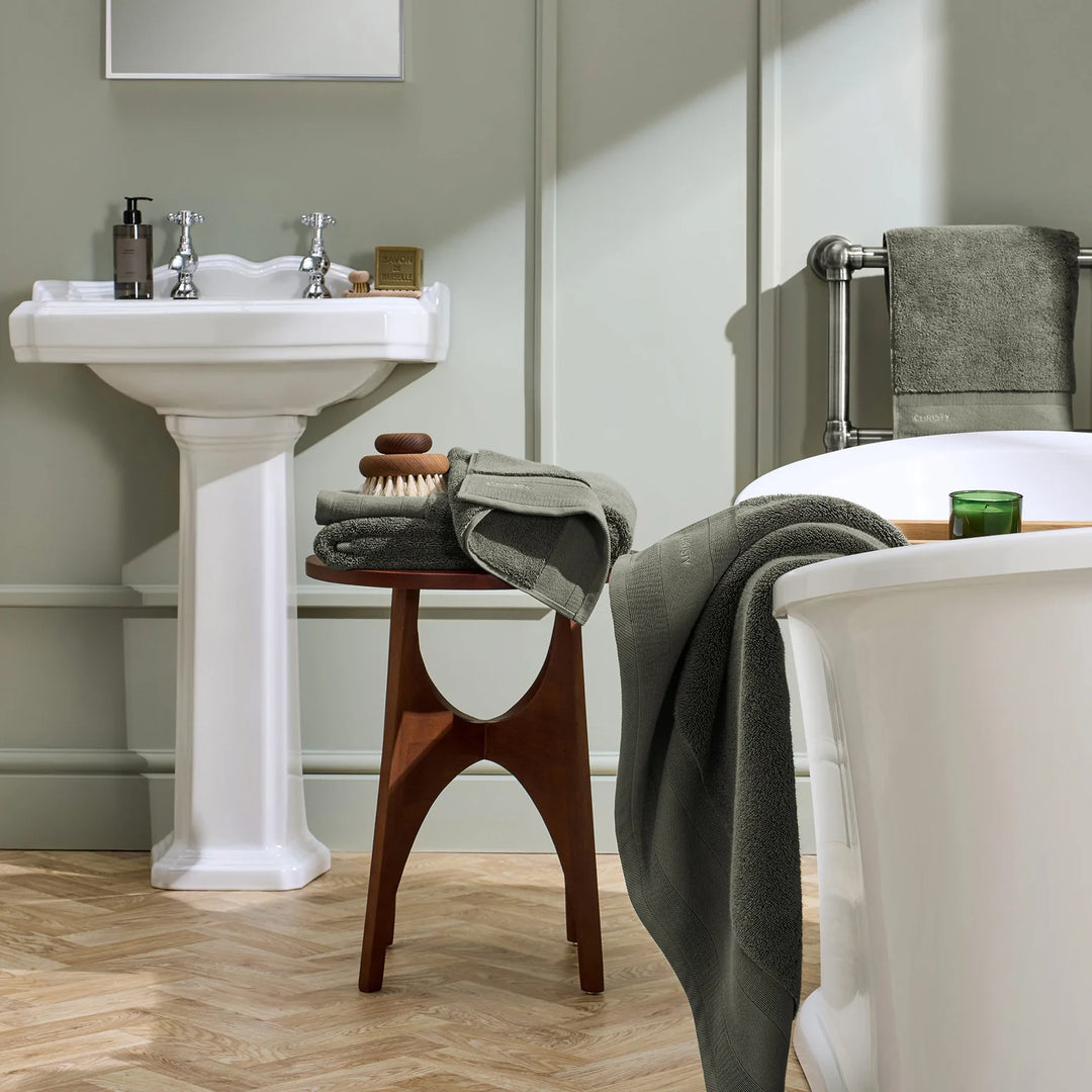 Bathroom with a sink, stool, and bathtub with towels.