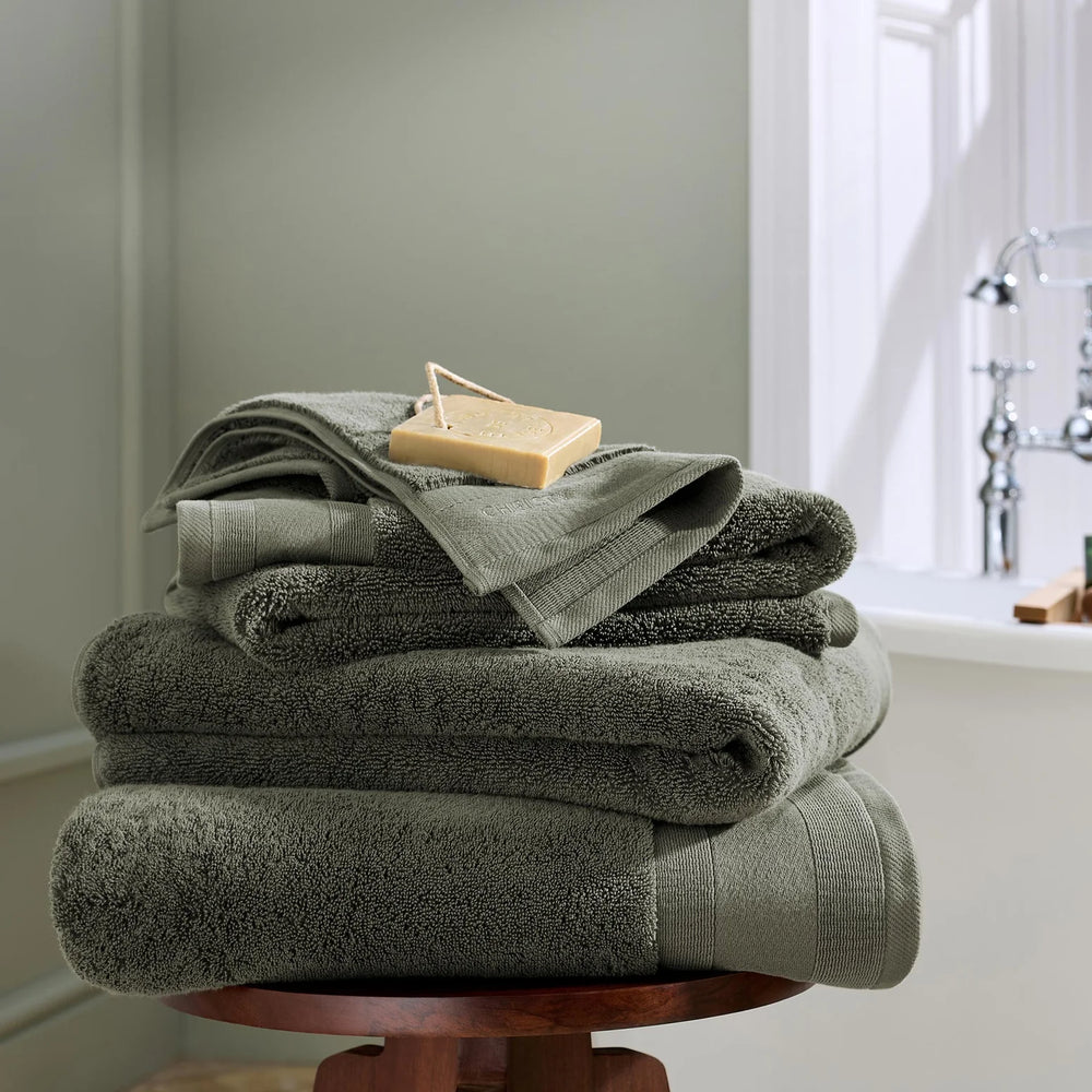 Stack of green towels on a wooden stool in a bathroom setting