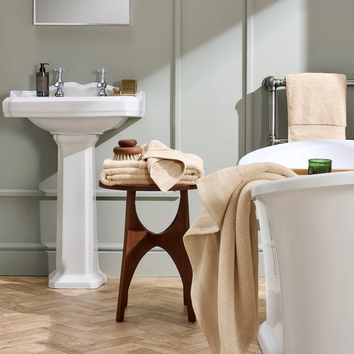Bathroom with a sink, bathtub, and wooden stool with towels and toiletries.