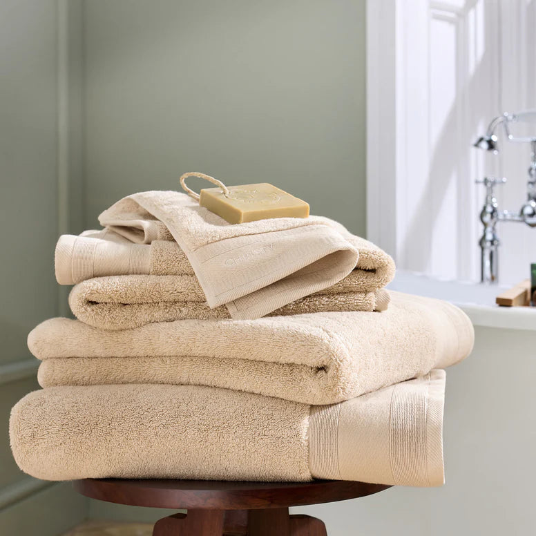 Stack of sand towels on a wooden stand with a bathroom setting in the background.