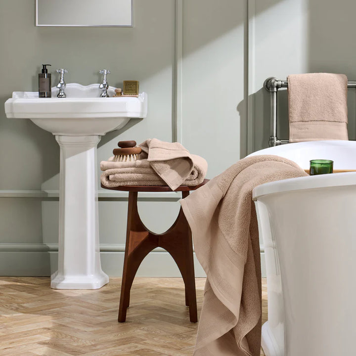Bathroom with a white pedestal sink, bathtub, and wooden stool with towels.