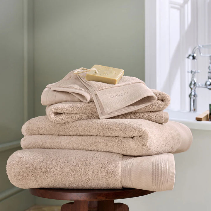 Stack of beige towels with a bar of soap on a wooden stand in a bathroom setting.