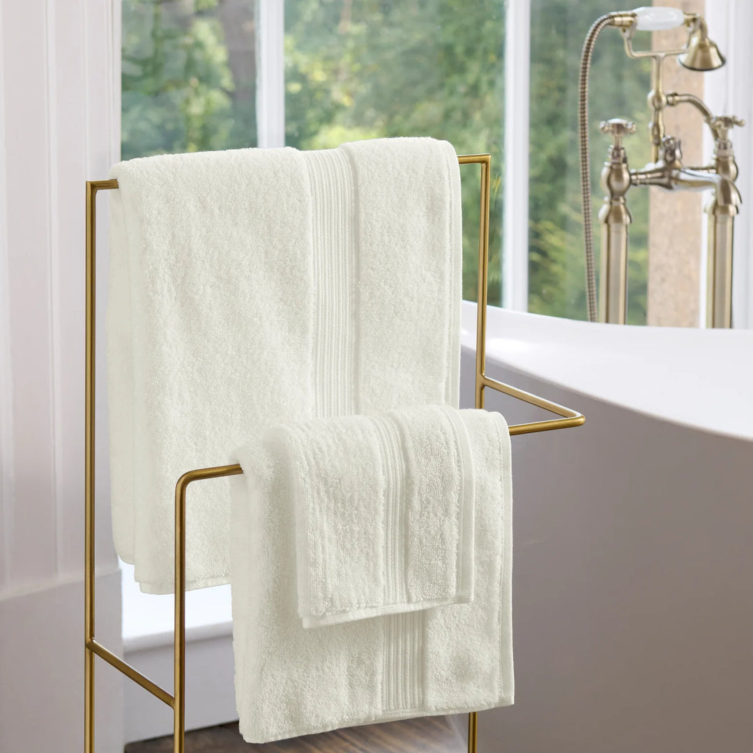 White towels on a gold towel rack in a bathroom with a window in the background.