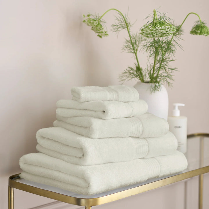 Stack of CHRISTY Supreme Hygro Towels - Almond on a gold shelf with a plant in the background