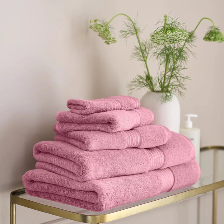 Stack of CHRISTY Supreme Hygro Towels - Blush on a gold tray with a vase of greenery in the background.