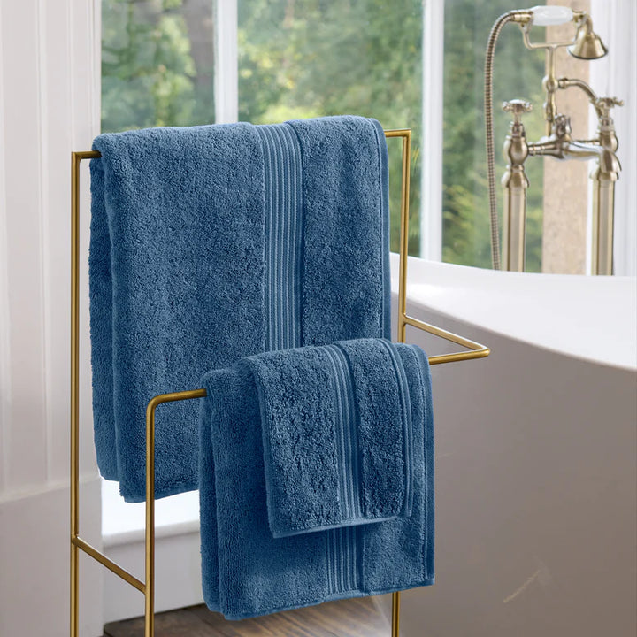CHRISTY Supreme Hygro Towels - Deep Sea hanging on a gold towel rack in a bathroom.