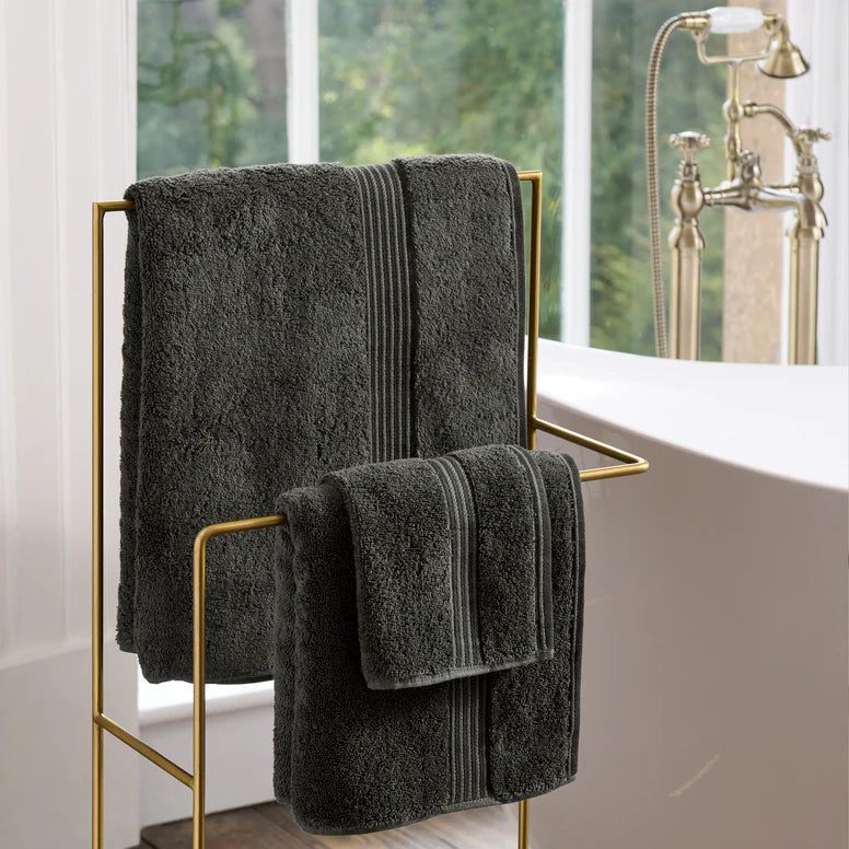 CHRISTY Supreme Hygro Towels - Graphite on a gold towel rack in a bathroom with a bathtub and window in the background.