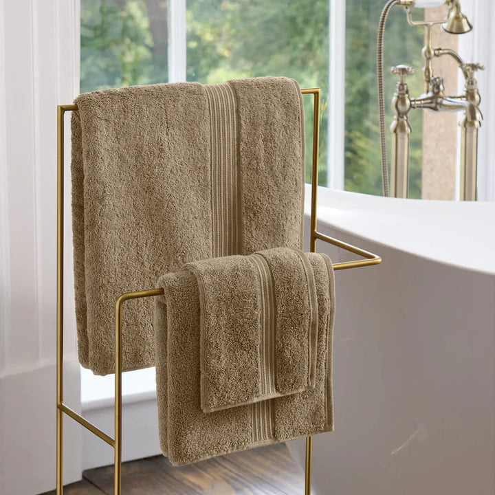 CHRISTY Supreme Hygro Towels - Mocha on a gold towel rack in a bathroom with a bathtub and window in the background.