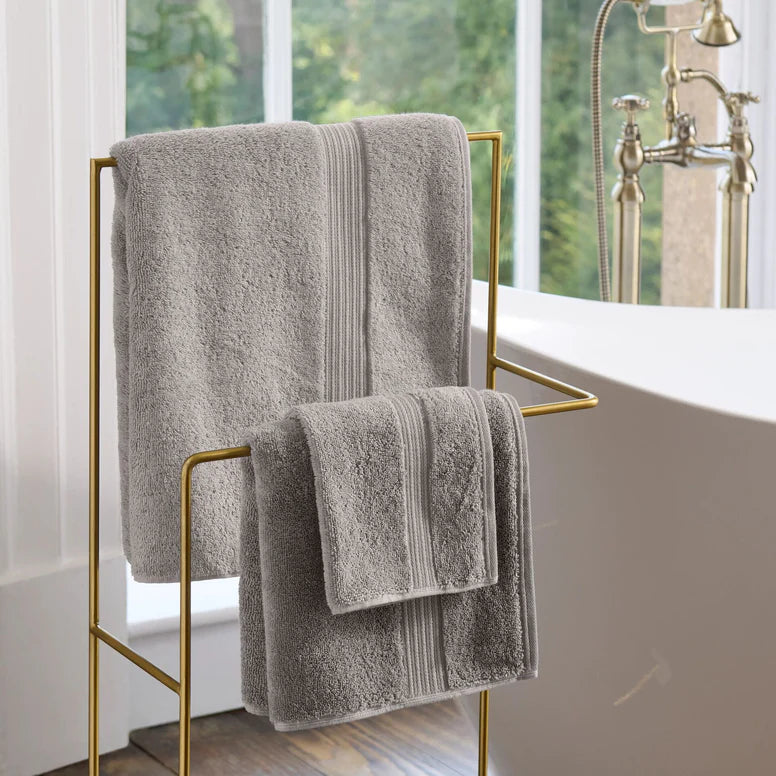 CHRISTY Supreme Hygro Towels - Silver hanging on a gold towel rack in a bathroom.