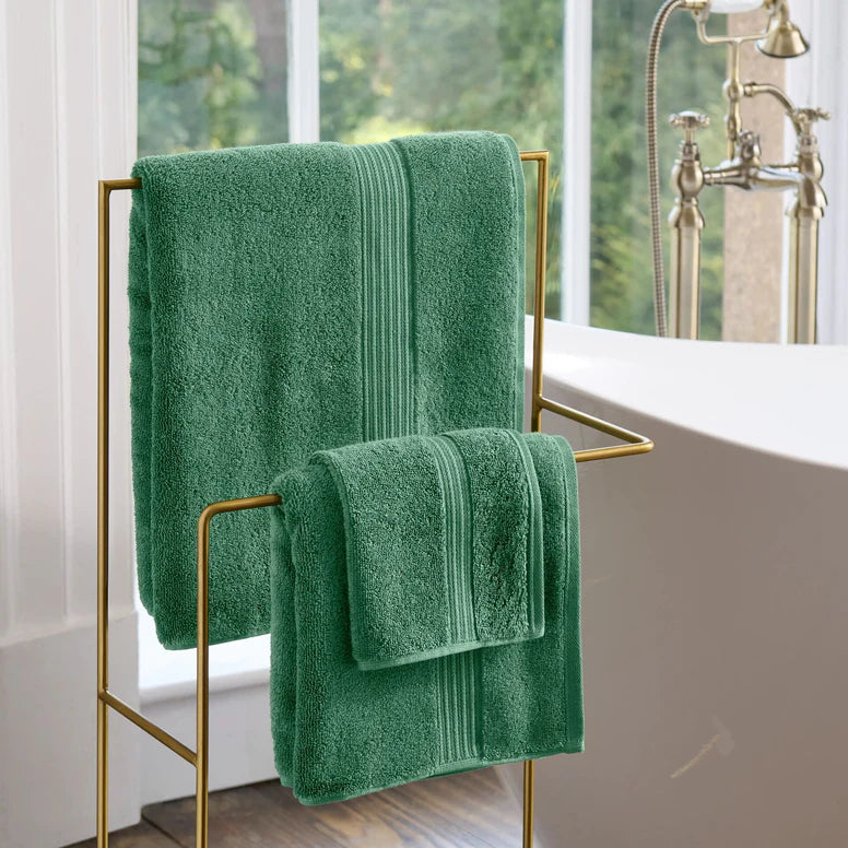 CHRISTY Supreme Hygro Towels - Spruce hanging on a gold towel rack in a bathroom.