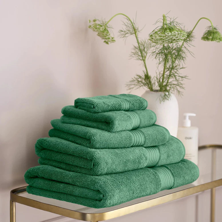 Stack of CHRISTY Supreme Hygro Towels - Spruce on a gold shelf with a plant in the background