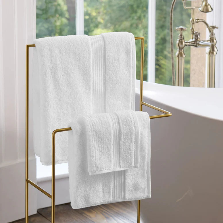 CHRISTY Supreme Hygro Towels - White on a gold towel rack in a bathroom with a bathtub and window in the background.