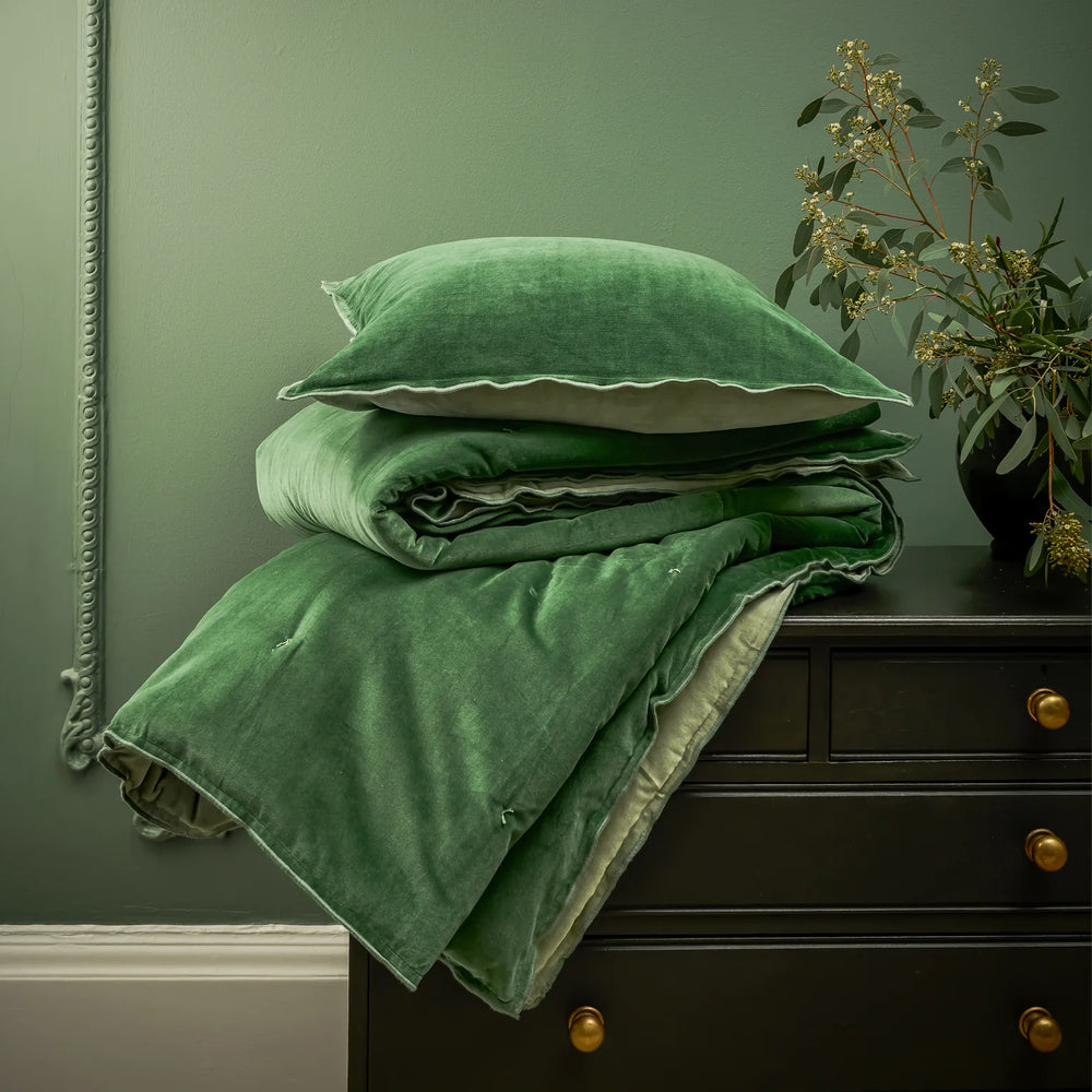 Green velvet bedding set on a dark dresser against a green wall.