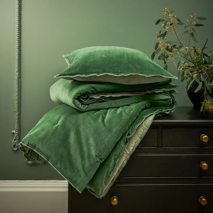 Green velvet bedding set on a dark dresser against a green wall.