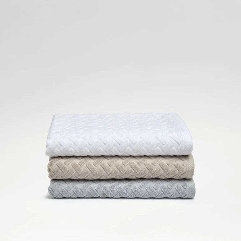 Stack of three quilted blankets in white, beige, and gray on a light gray background