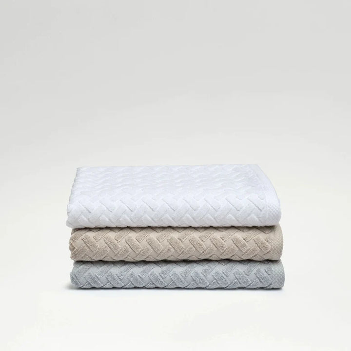 Stack of three quilted blankets in white, beige, and gray on a light gray background