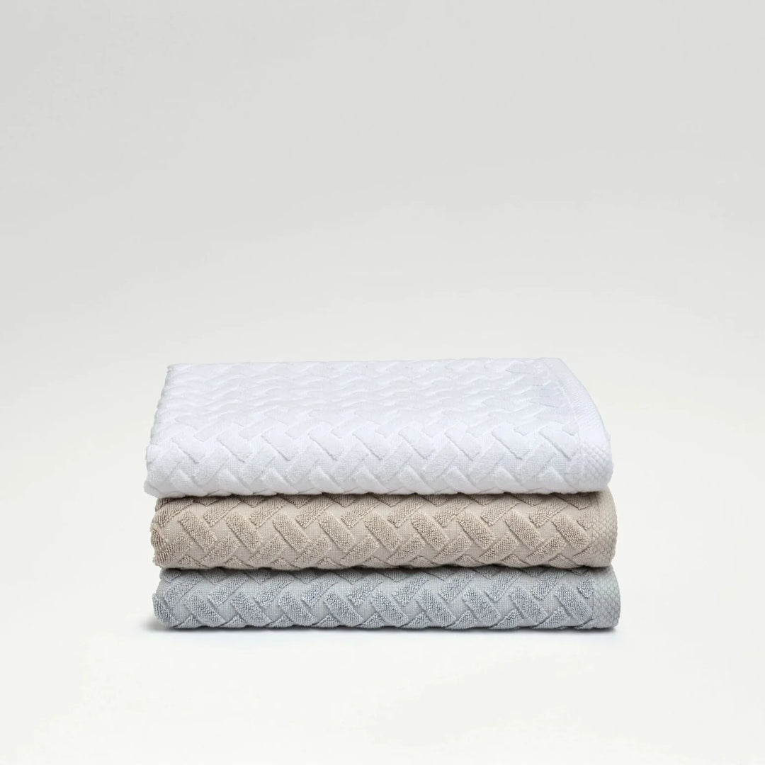 Stack of three quilted blankets in white, beige, and light blue on a light gray background