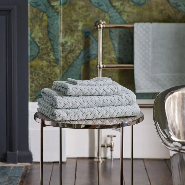Stack of CHRISTY Trellis Towels - Glacier on a round marble table with a decorative wall in the background