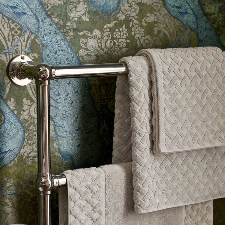 Towel rack with CHRISTY Trellis Towels - Oak against a decorative wall.