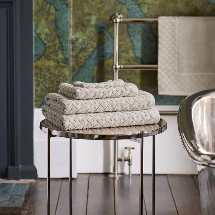 Stack of CHRISTY Trellis Towels - Oak on a round metal table with a decorative wall in the background