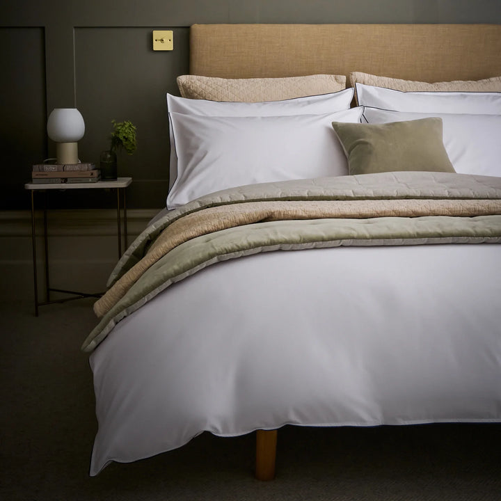 Neatly made bed with white bedding and beige blanket in a dimly lit room.