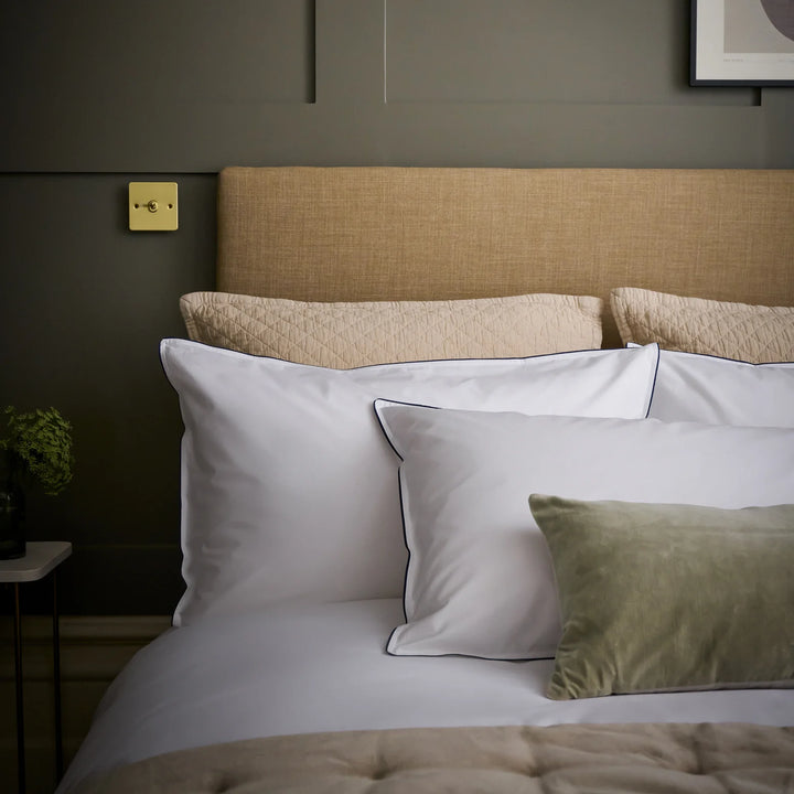Neatly made bed with pillows against a green wall