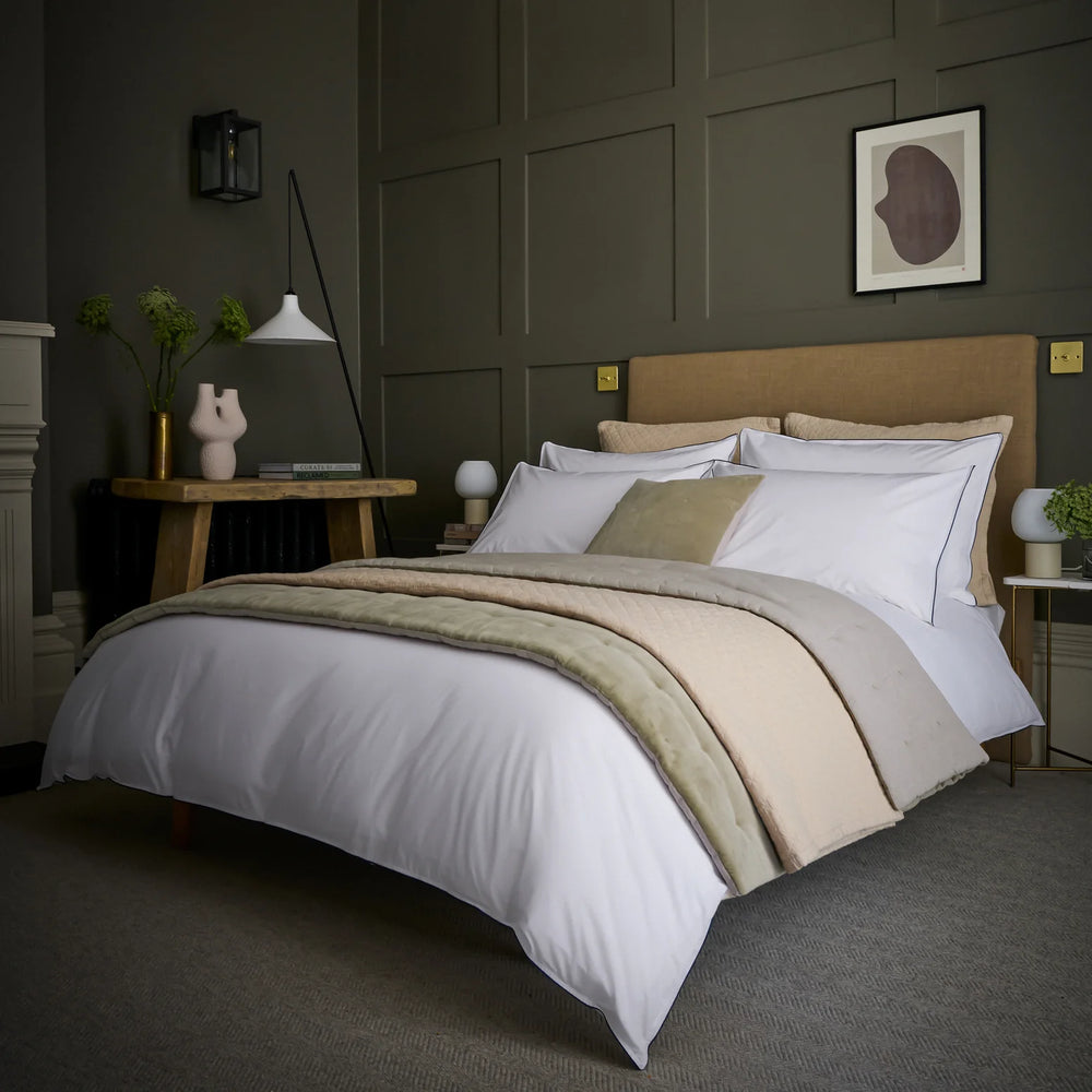 Neatly made bed with beige and white bedding in a bedroom setting.